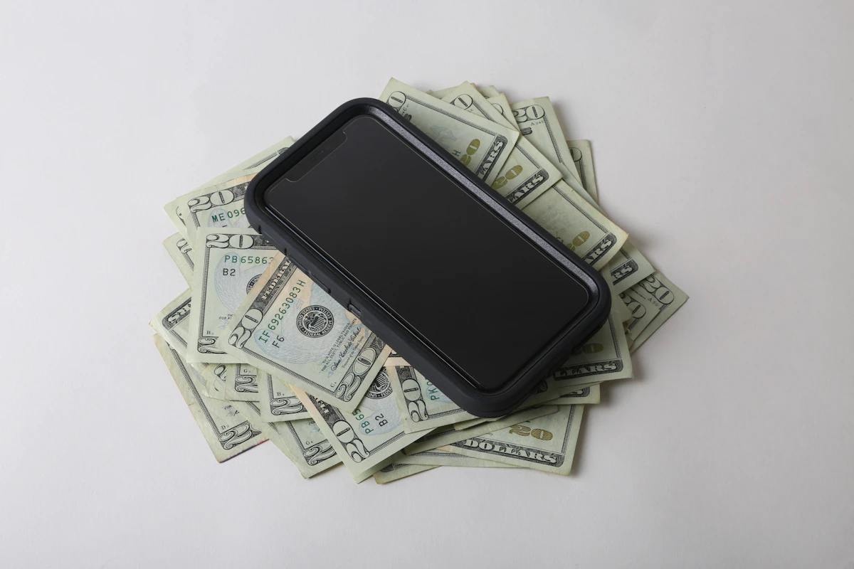 A smartphone lying on a pile of dollar bills